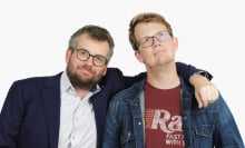 Hank and John Green in front of a white background, smiling at the camera.