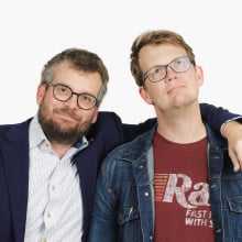 Hank and John Green in front of a white background, smiling at the camera.