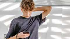 A teen boy looks down at his phone.
