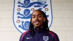Djed Spence smiling in front of a giant England badge.
