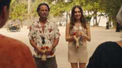 Walton Goggins and Aimee Lou Wood, in costume, stand next to each other on a beach in a scene from The White Lotus