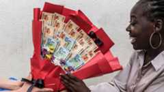 A woman smiles as she receives a bouquet made of banknotes and flowers from her boyfriend as a surprise ahead of Valentine's Day during a hangout in Kampala on February 7, 2026.