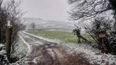 Rural view of farm track and rolling green fields covered in a light dusting of snow