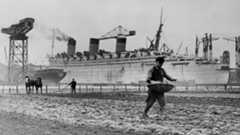 A black and white image of a large ocean liner with a large crane in the left of the shot and people sowing fields in the foreground