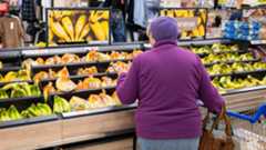 Woman in purple jumper picks up bananas on fruit aisle in Tesco