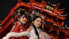 Women wearing traditional costumes pose for photographs in front of a Chinese temple