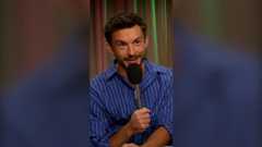 Jonathan Bailey holding a mic, wearing a blue stripy shirt.