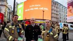 London Fire Commissioner Jonathan Smith stands in front of large billboards with two colleagues - one male and one female - either side of him
