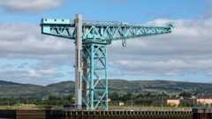 A large latticed steel crane with a lift shaft at itss side with hills in the background