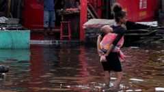 A girl carries an infant as she wades through water.