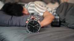 Man sleeping in bed and reaching for an analogue alarm clock
