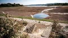Low water levels at Chew Valley lake - the photo shows a small pool of water amid a vast expanse of mud. In the distance the edge of the lake is ringed by forests