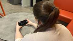 An actress with her back to the camera poses with a smart phone which shows graphs detailing the current rate of cryptocurrency.