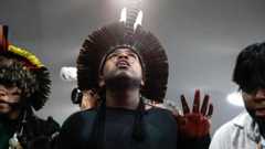 Indigenous people at a protest. Man in centre wears a headpiece made of features and red dye or ink on fingers