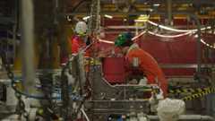 workers in orange overalls operate heavy machinery