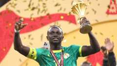 Sadio Mane, wearing a green Senegal shirt, lifts the Africa Cup of Nations trophy in his left hand