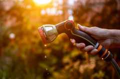 A hand holds a garden hose. A few water drips are seen coming from the hose