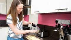 A woman pours cheese out of a food processor into a baking dish