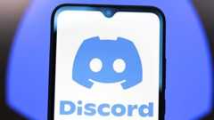 Discord logo shown on a smartphone screen in front of a larger, blurred version of the company's blue logo.