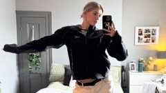 Emily with blonde hair tied back taking a selfie in her bedroom mirror with a stylish interior behind her