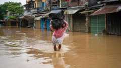 A man in a raincoat wades through the floodwaters in Hoi An, carrying two large packs of items wrapped in black trash bags