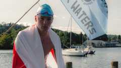 Hector Pardoe looks from boat on lake on with flag draped round him