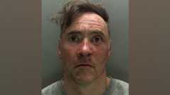 A police custody photo of Paul Doyle wearing a grey jumper and looking stunned. His hair, a long brown fringe, is dishevelled and to the side. His face has red marks on it