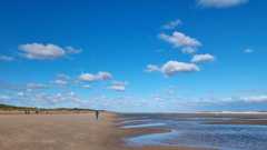 Bright blue sky with a few white clouds over a beach with the sea to the right