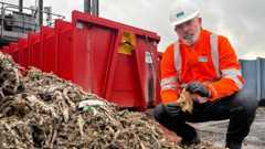 An employee of Severn Trent holds a soiled wet wipe in front of a pile of wet wipes.