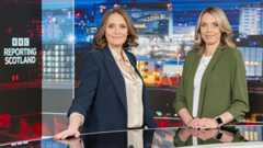 Laura Miller and Laura Goodwin standing behind the Reporting Scotland desk