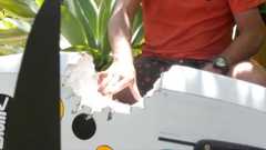 A shark teeth-sized bite in a wind surfboard next to a man with an orange shirt