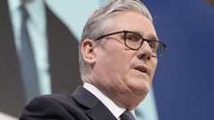 Prime Minister Starmer speaking at the conference. He is wearing a black suit and white shirt with a dark-coloured patterened tie.