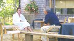 A copy of an undated picture of Peter Mandelson sitting in a white robe laughing while sitting opposite Jeffrey Epstein, who wears a blue top and cream chinos, on a wooden deck.