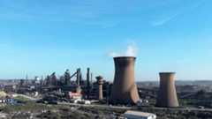 A landscape image of the British Steel works against a blue sky. Two large chimneys can be seen in the foreground - smoke is coming out of one.