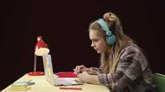 Teenage girl on her laptop. She is wearing headphones and is studying.