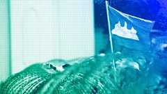 FILE: A Cambodian flag flutters above barbed wire set up by police near the Council of Ministers building while garment workers gather for a rally in Phnom Penh, December 2013