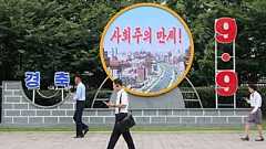 Люди идут по району Тэдонган в Пхеньяне перед плакатом с надписью "Да здравствует социализм" 9 сентября 2025 года.