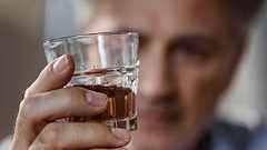 Ein älterer Mann hält eine Flasche Schnaps.