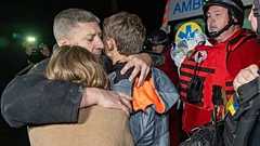 Un homme prend ses enfants dans ses bras alors qu'ils réagissent à la mort de leur mère, tuée par une frappe aérienne russe