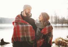 Couple looking each other near winter lake under plaid