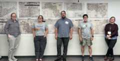 5 individuals standing in front of two rows of color coded maps.