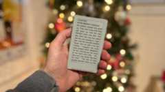 The Xteink X4 e-reader held in one hand displaying an ebook, with an out of focus Christmas tree in the background