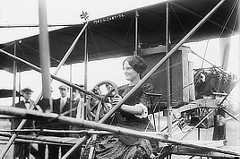 Photo shows a woman sitting in the cockpit of a biplane.