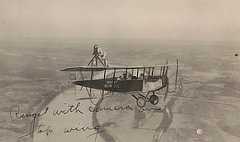 Photo shows biplane flying above a curving river and flat land below.
