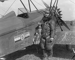 Photo shows a pilot wearing heavy clothing and goggles while standing beside the plane.