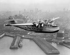 Photo shows a seaplane flying above the San Francisco harbor.