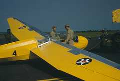 Photo of a glider painted yellow with two soldiers looking at the cockpit.