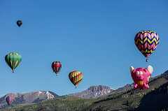 Color photo shows balloons in flight with mountains in the background.