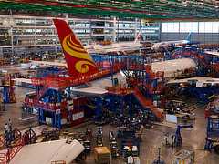 Color photo shows the tail fin area of a large airplane being put together in a commercial warehouse.