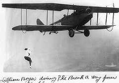 Photo shows a woman hanging from the wing of a biplane.